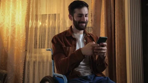 Young man in a wheelchair using his phone and smiling. Disabled guy texting  Stock Footage 202117489