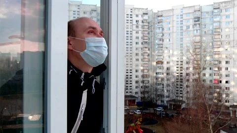 A young man in white blue protective disposable medical mask walks on balcony Stock Footage 152565826