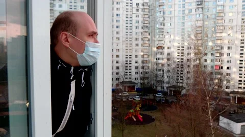 A young man in white blue protective disposable medical mask walks on balcony Stock Footage 152565840