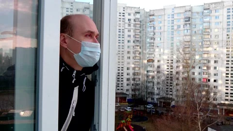 A young man in white blue protective disposable medical mask walks on balcony Stock Footage 152565869