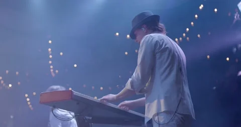 A young man in white clothes plays a synthesizer on stage. Rock band live Stock Footage 151755906
