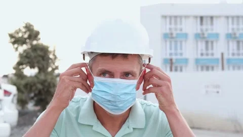 A young man in a white construction helmet puts on a medical mask. Stock Footage 166392550