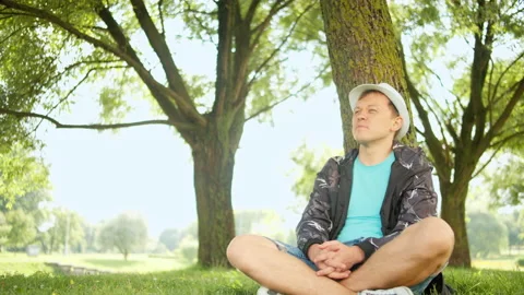 Young man in white hat on a sunny day sitting with a mobile phone under a tree Stock Footage 139410862