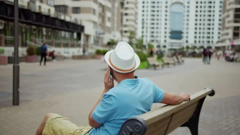 Young man in white hat talking on the phone while sitting on a bench Stock Footage 140408403
