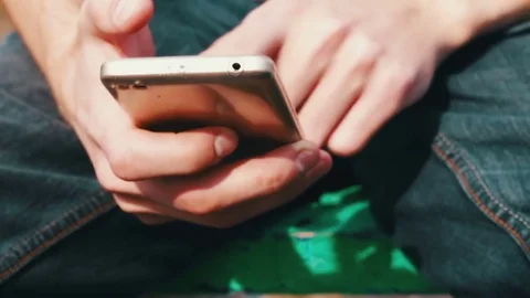Young man with white phone sits in spring on street, in park, outdoor Stock Footage
