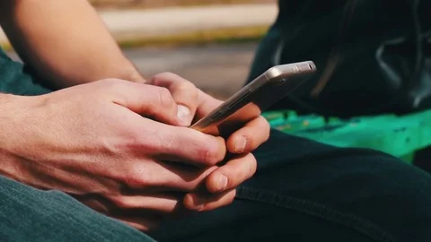Young man with white phone sits in spring on street, in park, outdoor Stock Footage