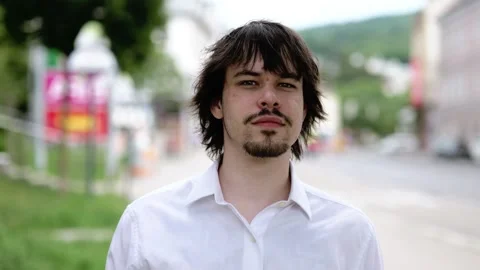 Young man in a white shirt thoughtfully looks into the distance on a city street Stock Footage 336786238