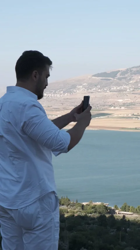Young man in white taking a vertical video of the natural dam Stock Footage 229691362