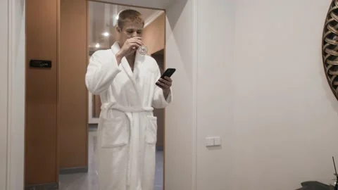 A young man in a white terry bathrobe in a spa salon with a glass of champagne Stock Footage 172582526