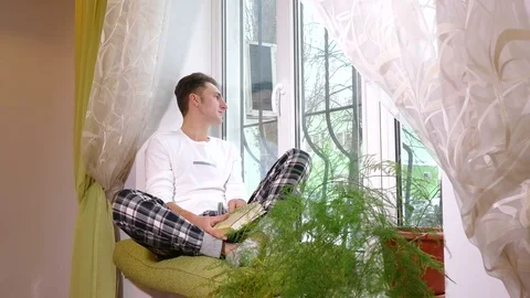 Young man on the windowsill and looking at the window Video stock 71779527