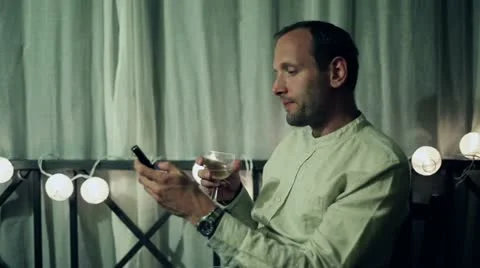 Young man with wine and cellphone relaxing on his balcony in the evening Stock Footage