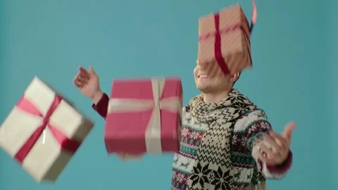 A young man in winter clothes on a blue background throws gift boxes. Video stock 226219123