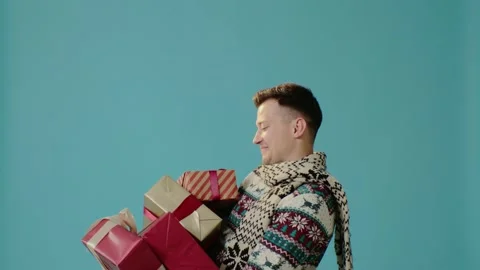 A young man in winter clothes on a blue background throws gift boxes. Stock Footage 226219211