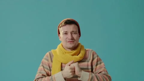 A young man in winter clothes on a blue background blows on hands, feels cold. Stock-Footage 226220030