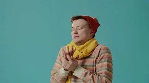 A young man in winter clothes on a blue background blows on hands, feels cold. Stock-Footage 226220044