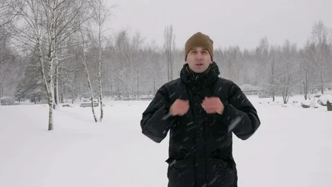 A young man in winter is cold in the forest. Big snowfall. He's breathing on his Stock Footage 71217948