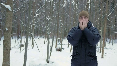 A young man in winter forest freeze. He's breathing on his hands, rubs and wears Stock Footage 71205385