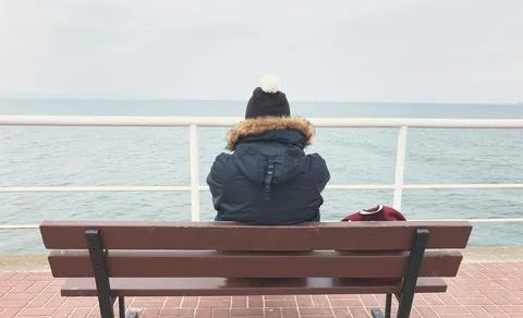 A young man in winter in a jacket, a hat and a backpack stands on the pier and Stock Photos