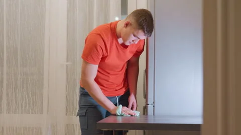 Young Man Wiping Kitchen Table With Green Cloth During Cleaning Routine Stock Footage 319920005