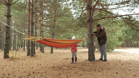 A young man in the woods sets hammock. Daughter walks nearby. Stock Footage 97150784