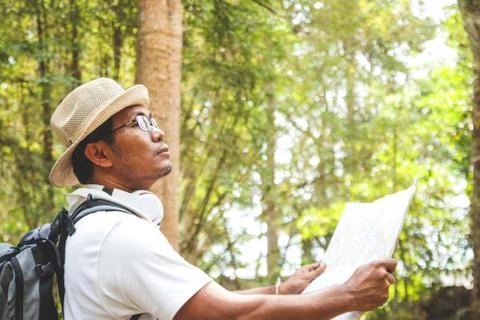 The young man wore a hat, backpack, standing, holding a map in the forest. Photos
