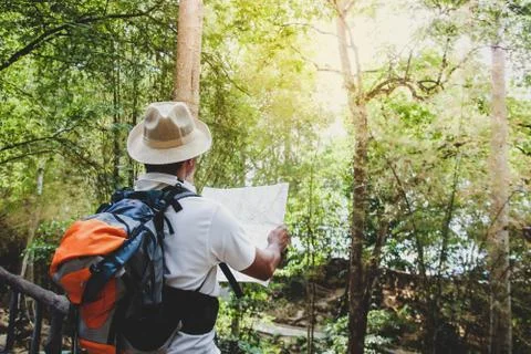 The young man wore a hat, backpack, standing, holding a map in the forest. Stock-Fotos