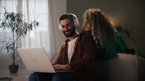 Young man work remotely using laptop sitting at couch.Bearded guy wear Stock Footage 212317896