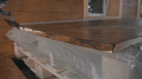 Young man in work uniform and gloves covers the ribs of a wooden tabletop Vidéo 145260586