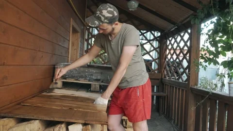 A young man in a work uniform and gloves covers the wooden shelves with a brush Vidéo 145260619