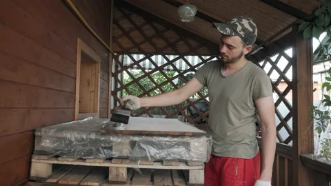 Young man in work uniform and gloves covers the wooden tabletop with a brush Vidéo 145260653