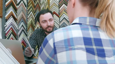 Young man worker chatting with customer about picture frame details, using Stock-Footage 121985030