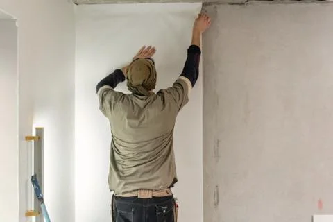 Young man, worker glueing wallpapers on concrete wall. Repair the apartment Stock Photos