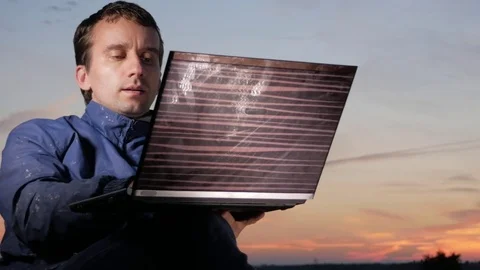 A young man is working behind a laptop at sunset. Beautiful sky behind. Stock Footage 76923250