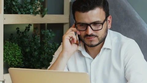 Young man working in cafe with laptop and talking on his phone Stock Footage 112989100
