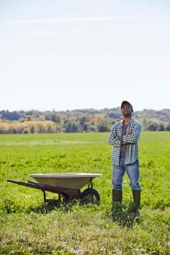 A young man in working clothes standing in a crop field with arms folded next to Stock Photos
