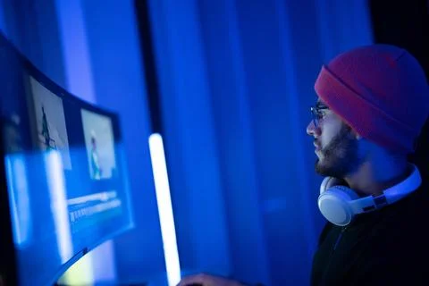 Young man working on a computer in a cozy gaming setup with blue lighting i.. Stock Photos