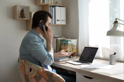 Young man working on computer with documents, talking on phone. Foto stock