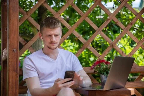 Young man working on computer laptop typing on mobile phone on summer morning Stock Photos