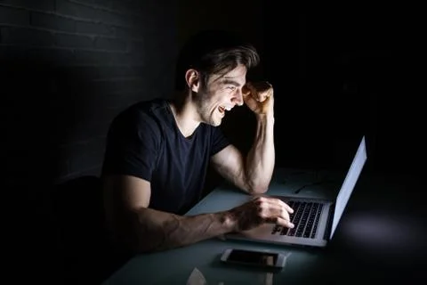 Young man working on computer at night in dark office the designer works in t 写真素材