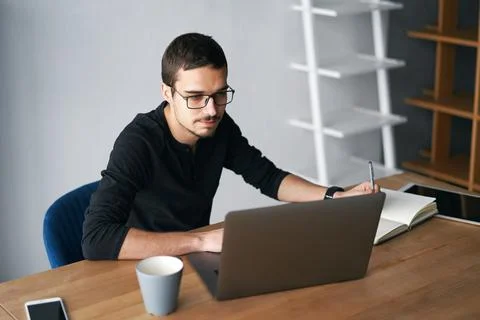 Young man working with computer, phone and tablet at the table while drinking Stock Photos