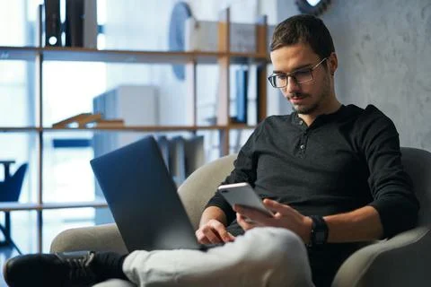 Young man working with computer, phone and tablet at the table while drinking Stock Photos