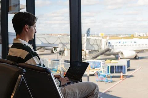 Young man working on a computer while waiting in an airport terminal area. Stock Photos