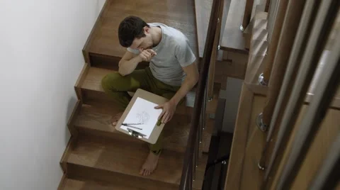 Young man working on a drawing sitting on the stairs in the cottage 2 Stock Footage 45429930