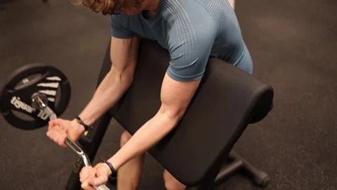 A young man is working on his biceps at the gym, focusing on building strength a Vídeos de archivo 301677290