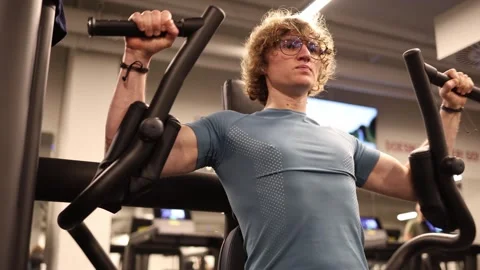 A young man is working on his chest at the gym, using a machine to bring his arm Stock Footage 301677211