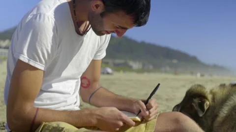 Young man working in his journal looks out over the ocean Stock Footage 52258310