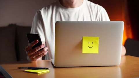 Young man is working on his laptop and checking notifications on his phone. Video stock 245360367