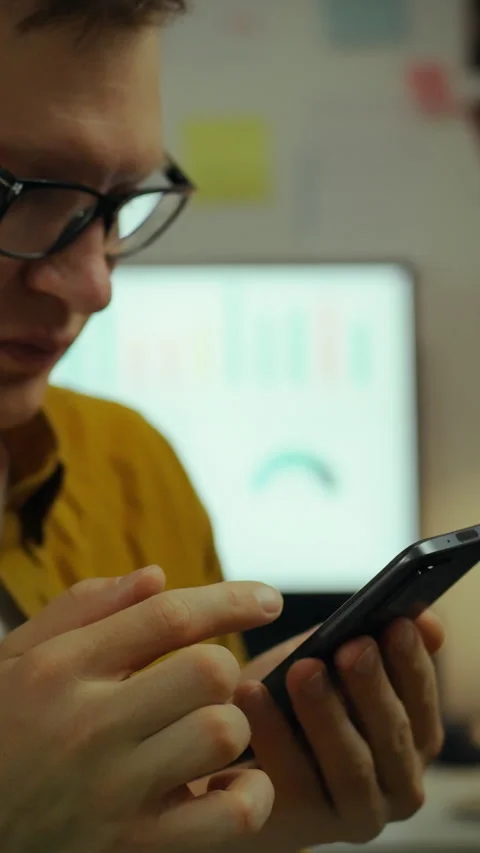 Young man working in home office at night while using smartphone amidst clut Stock Footage 331742352