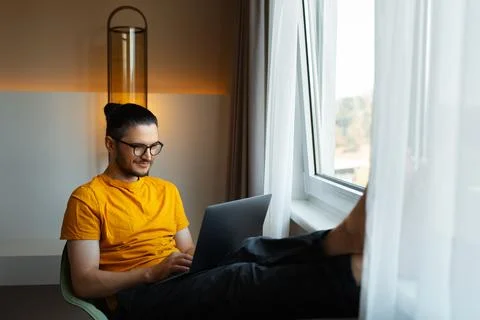 Young man working from home. Sitting on chair with laptop on legs. Wear eye.. Stock Photos