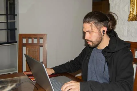 Young man working from home using laptop and wireless earphones Stock Photos
